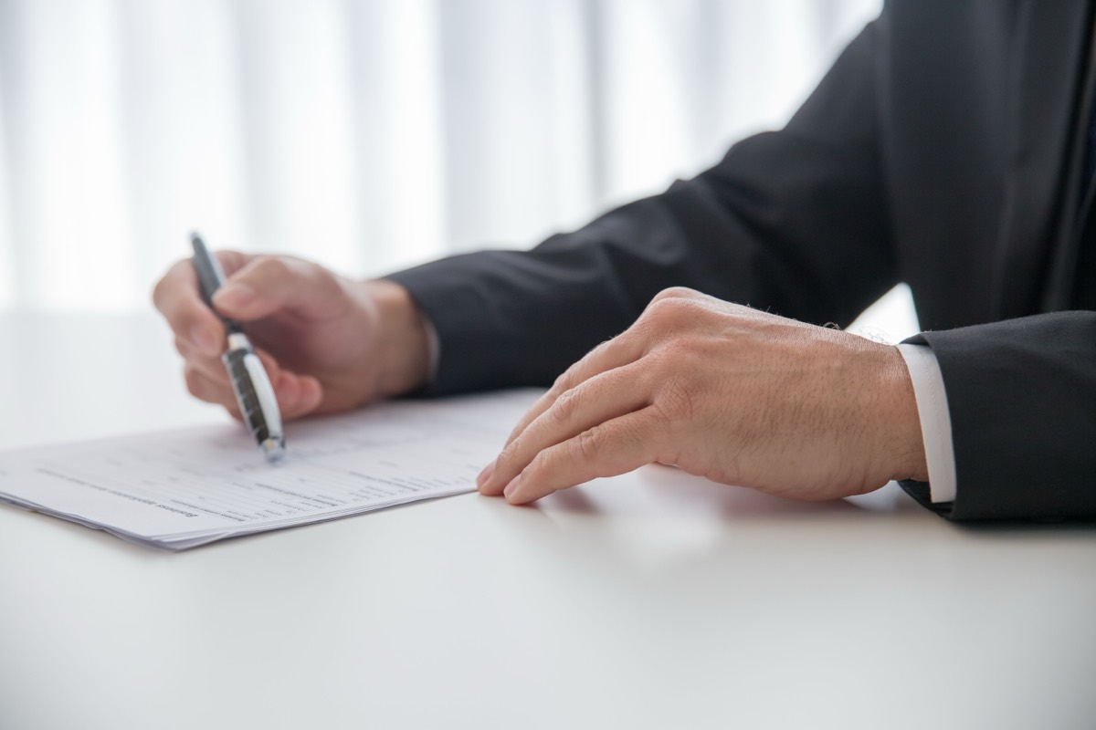 A man in a dark suit holding a pen over a printed form on a white desk, the kind of paperwork behind a Form FC filing with a bank in India