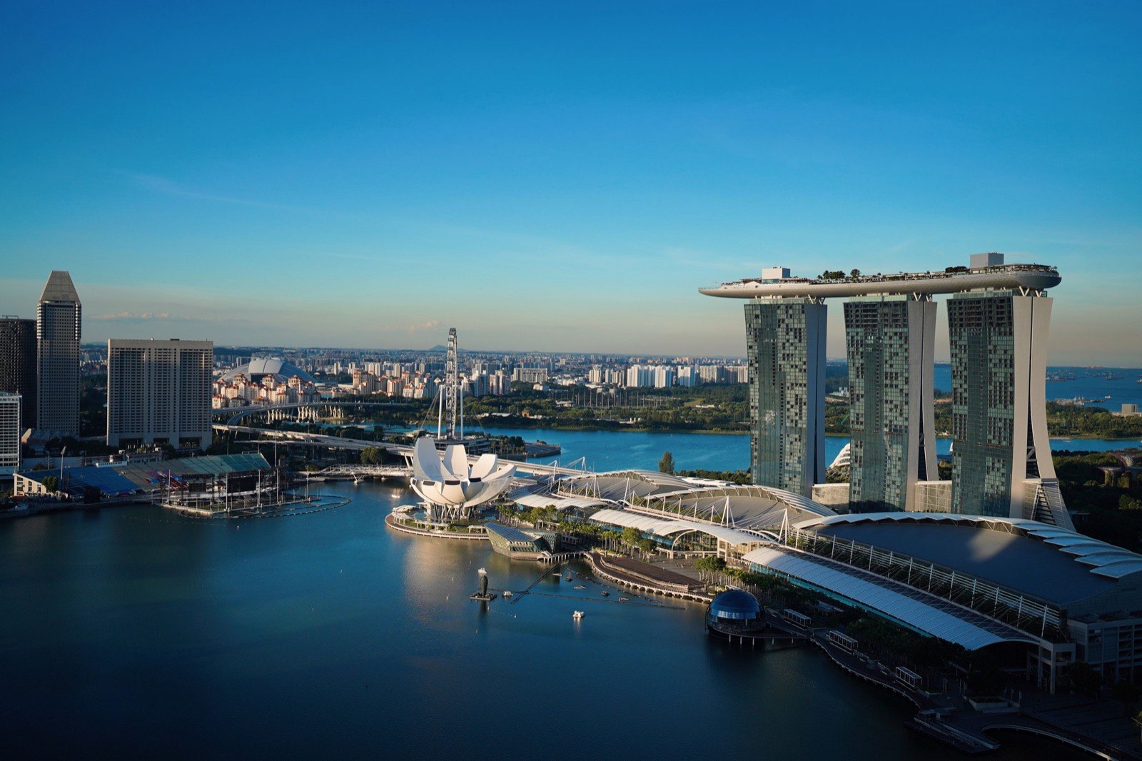 Aerial view of Marina Bay in Singapore on a clear afternoon, with the three hotel towers and their rooftop deck, the lotus shaped museum and the bay, the city this guide compares with Dubai as a base for a new company