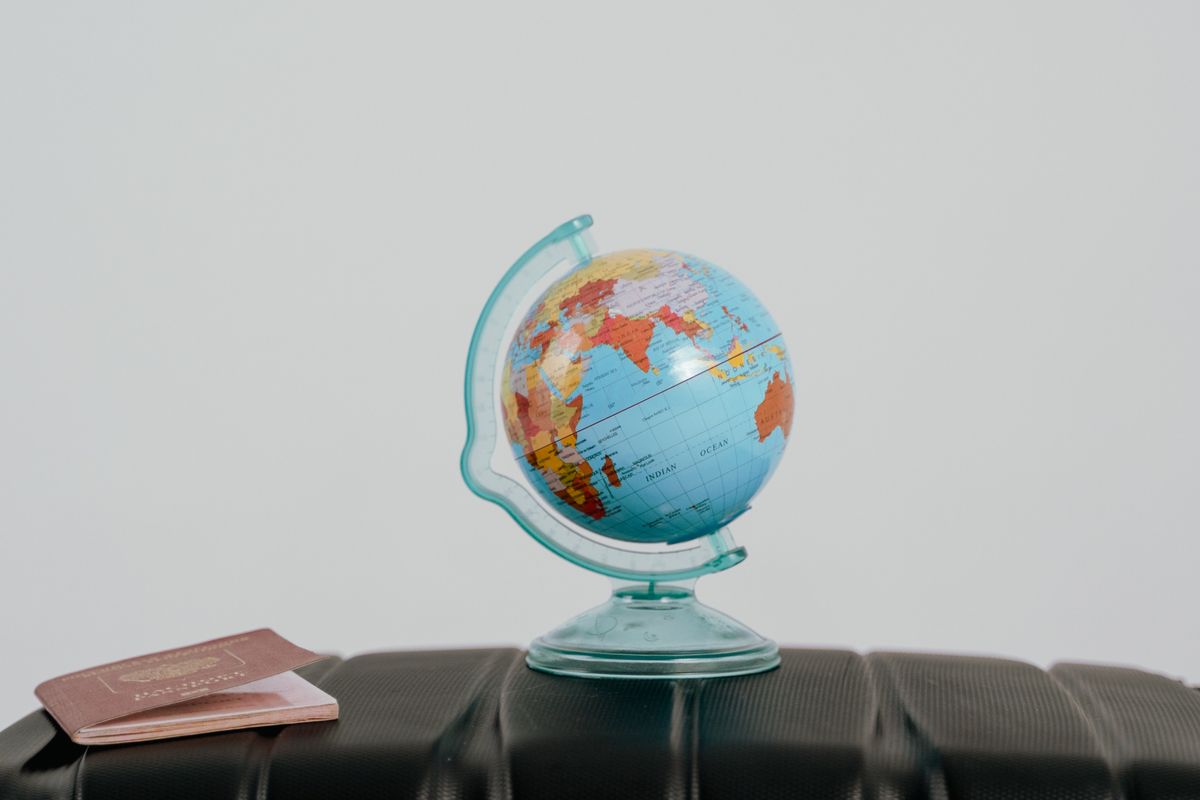 A small desk globe turned to the Arabian Peninsula and the Indian Ocean, standing on a black suitcase beside a passport, the planning that comes before a move to the UAE