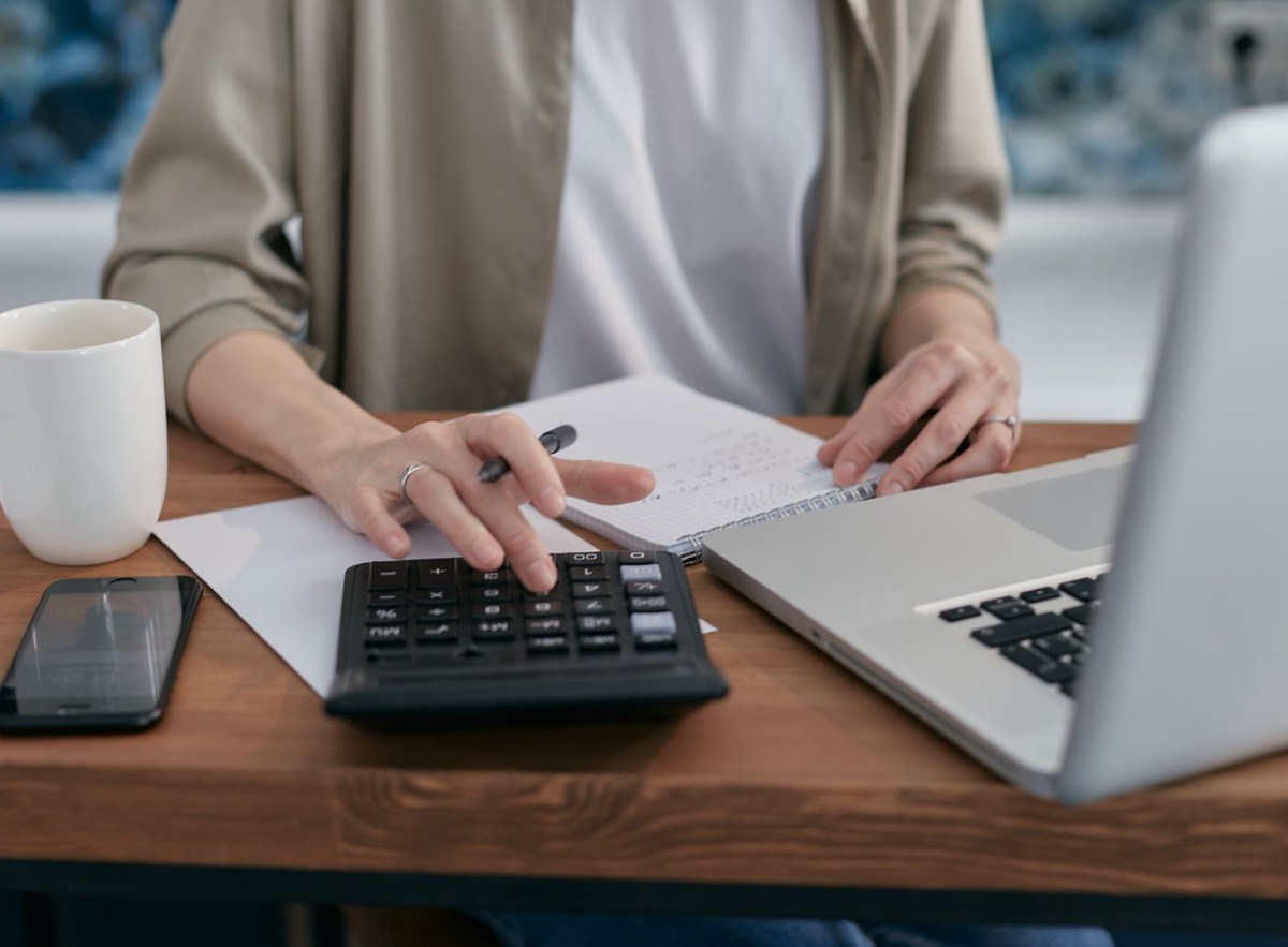 A person at a wooden desk using a calculator beside a notebook, laptop and phone, the kind of desk work involved in checking UK tax residence before leaving