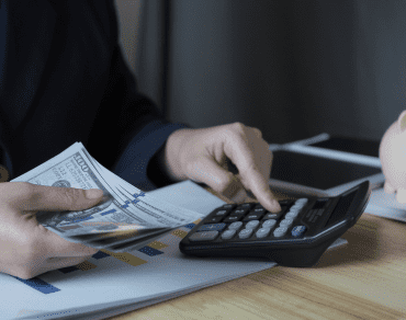 Counting banknotes beside a calculator while working out a monthly minimum balance